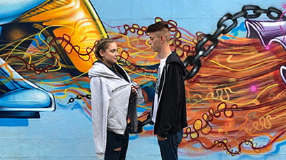A man and a woman stand in front of some street art.