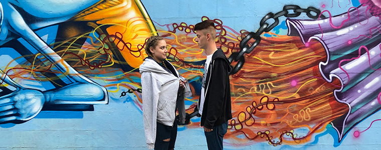 A man and a woman stand in front of some street art