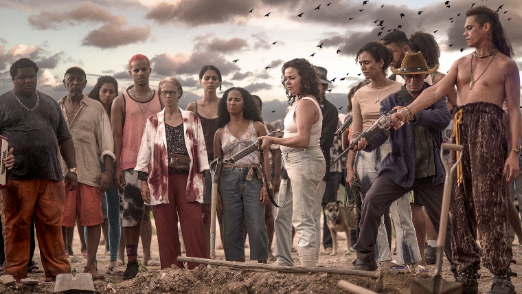 Cinematic scene of group of 15 people stood around earth mound, some holding pistols.