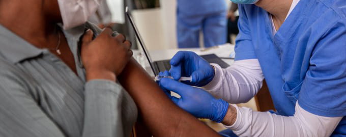 A person in blue scrubs giving an injection into arm of patient