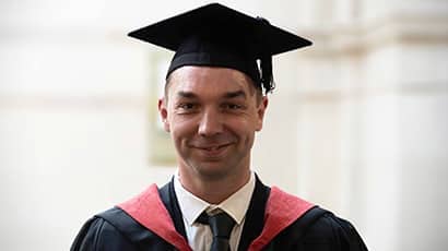 A man smiling at the camera wearing a graduation cap and gown