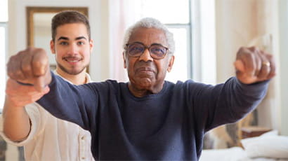 Healthcare worker and older person exercising together.