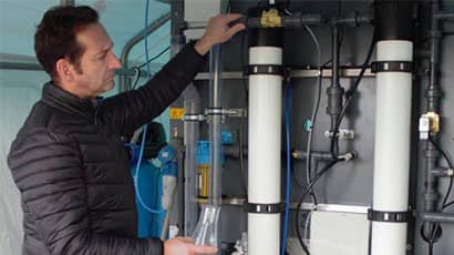 Man examining two large wall-mounted metallic cylinders.