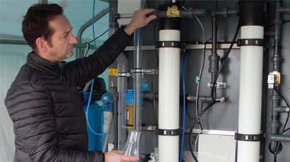 Man examining two large wall-mounted metallic cylinders.