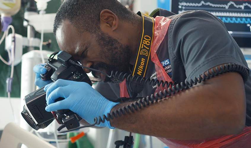 Man focusing as he takes a photograph using an SLR camera in a clinical setting