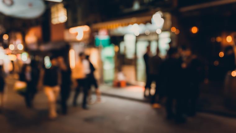 Blurred night time city scene of people walking and standing outside bars
