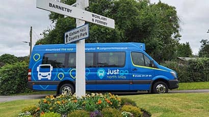 A blue minibus with grass and a flowerbed in the foreground