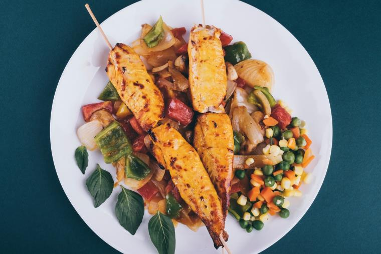 Plate with protein skewers on top of a bed of multi-coloured vegetables.