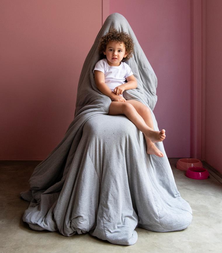 Baby sat on a shrouded figure against dark red backdrop