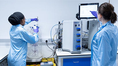 Two technicians in light blue overcoats working with lab equipment.