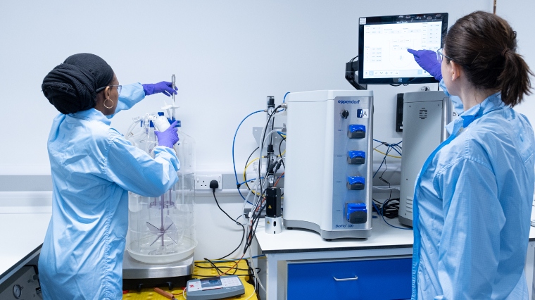 Two technicians in light blue overcoats working with lab equipment.