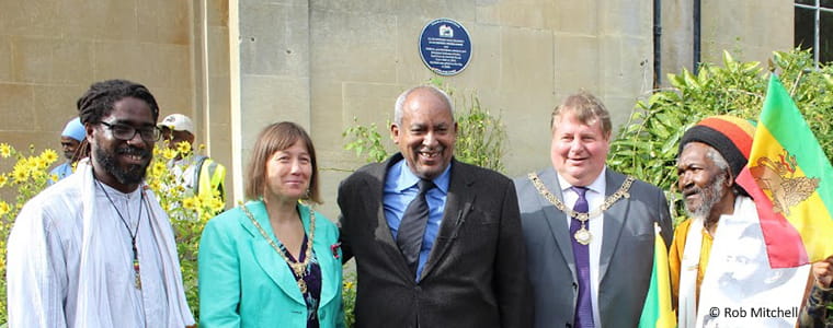 A small group of people posing in front of Fairfield House with blue plaque visible on the wall behind.