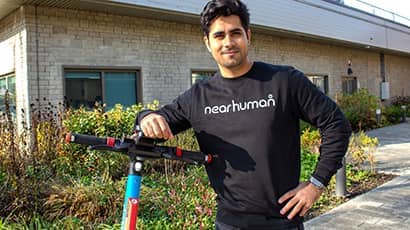 UWE Bristol graduate Faizan Mir standing with a rental e-scooter outside a university building