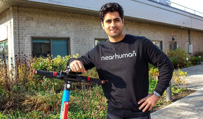 UWE Bristol graduate Faizan Mir standing with a rental e-scooter outside a university building