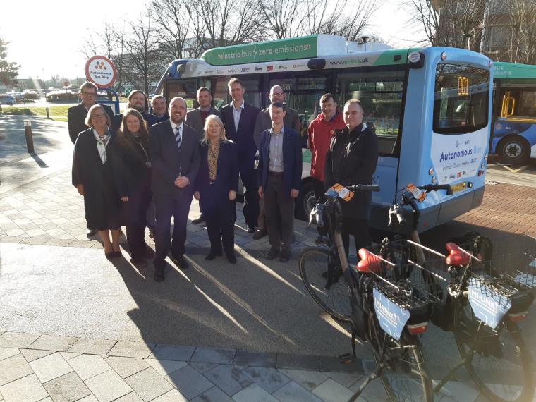 Group of people in suits standing in front of automated zero emissions bus smiling to camera