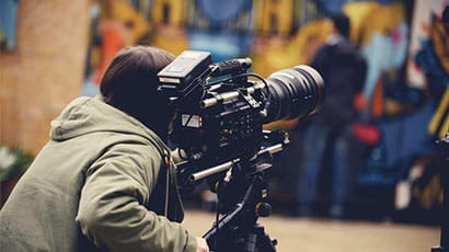 Camera person adjusting large film camera with graffiti scene in backdrop.