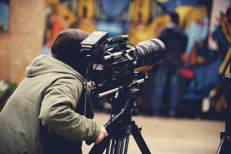 Camera person adjusting large film camera with graffiti scene in backdrop.