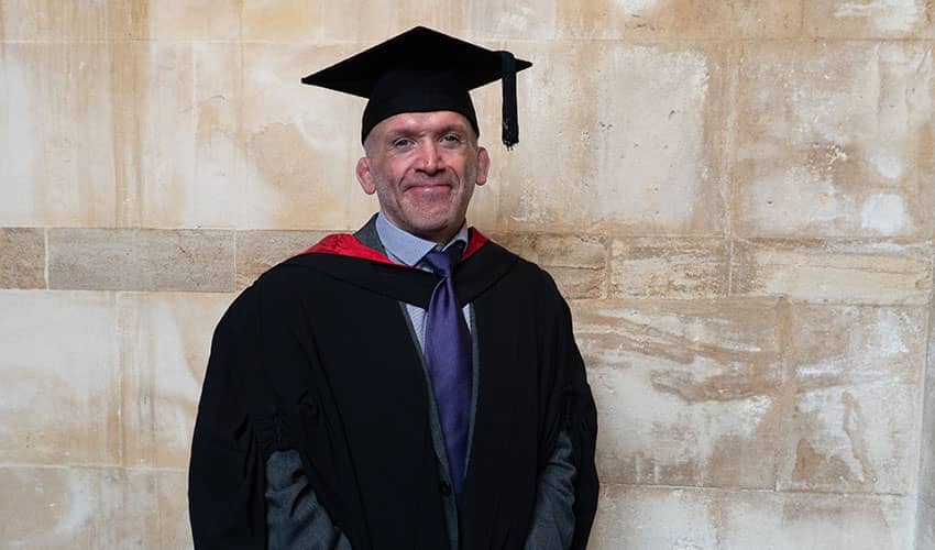A man wearing graduation robes and cap smiling at the camera