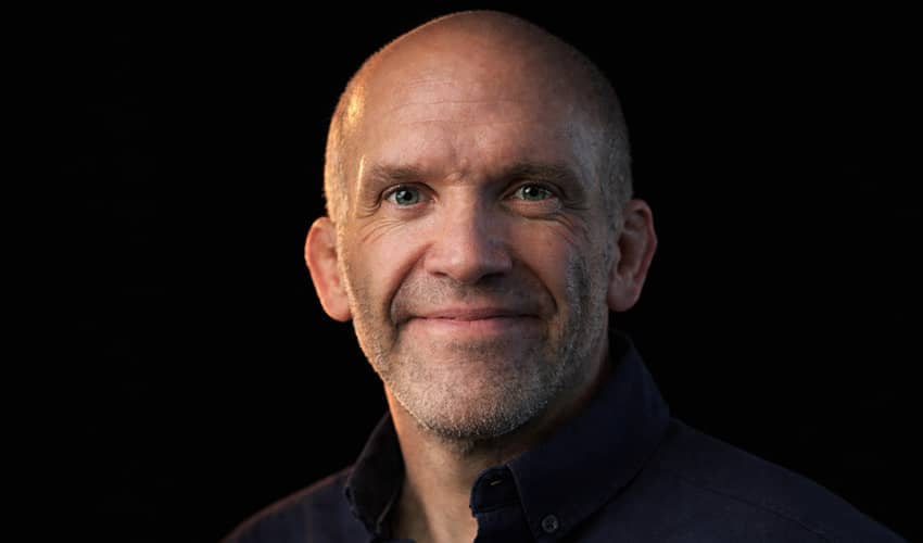 Head and shoulders photo of a person smiling at the camera, with a black background