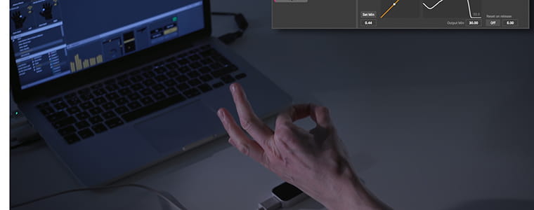 A hand shaped with finger and thumb together in front of a laptop screen.