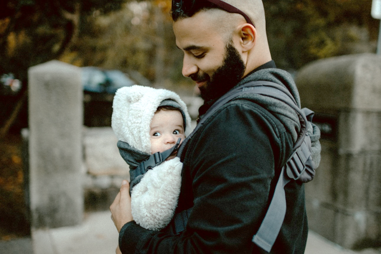 Man looking down affectionately at a baby he is carrying in a baby carrier sling