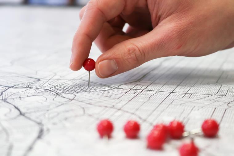A hand placing red pin onto a map