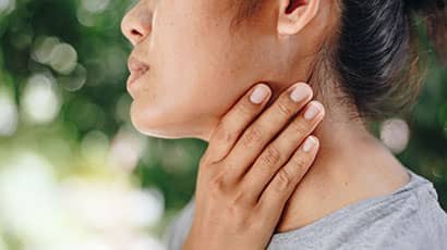 A side profile image of a woman with one hand holding her neck, with blurred greenery in the background