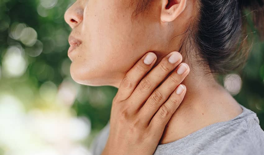 A side profile image of a woman with one hand holding her neck, with blurred greenery in the background