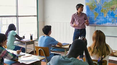 Image showing a man looking at a world map on the wall, teaching a group of secondary school children in a classroom