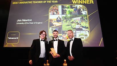 Three men wearing suits at an award ceremony, against a black digital screen with text on it