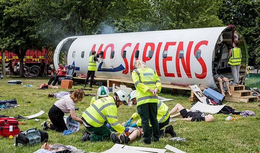 An emergency simulation scene showing a mocked up crash scence with an aircraft fuselage in the background, and emergency workers tending to pretend casualties in the foreground