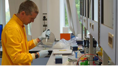Man in yellow lab coat using pipet.