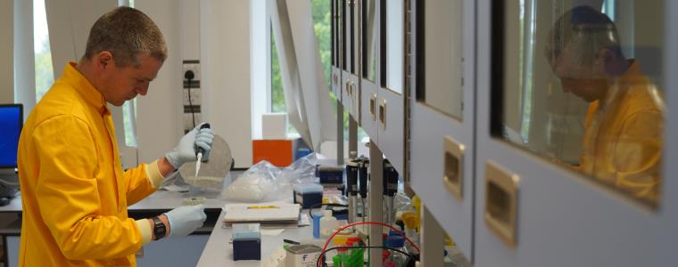 Man in yellow lab coat using pipet.