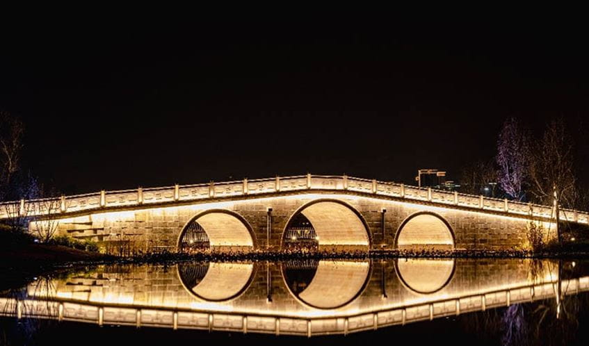 Illuminated bridge in darkness, with light reflected on a river