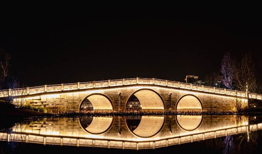 Illuminated bridge in darkness, with light reflected on a river