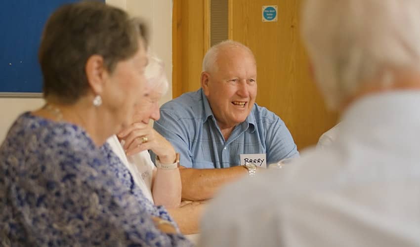 Photo of a dementia support celebration event, showing four people sat around a table
