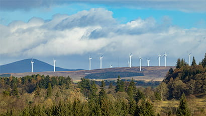 Wind turbines on an open hill, with woodland in the foreground