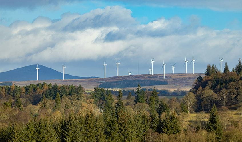 Wind turbines on an open hill, with woodland in the foreground