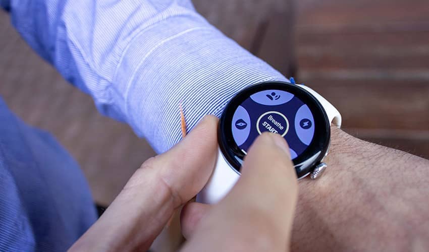 A close up image of fingers pressing a smartwatch which is displaying the word 'breathe'