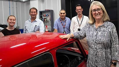 Five people smiling at the camera stood around a red Mini car