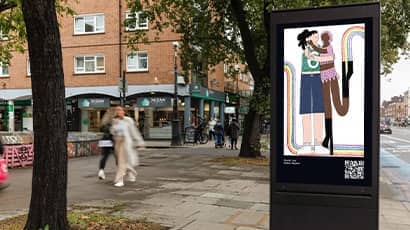 A street in Bristol shows people walking past a marketing board with a piece of eye catching artwork. 