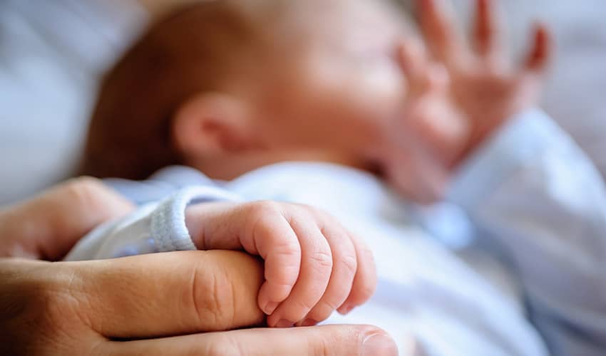 A newborn baby holding the hand of a parent