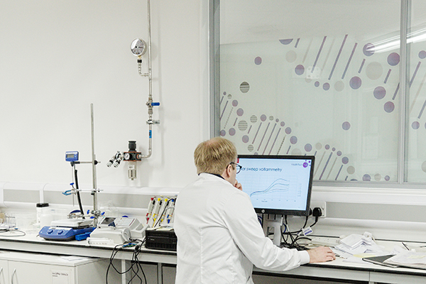 A researcher wearing white coat looking at computer screen in a lab