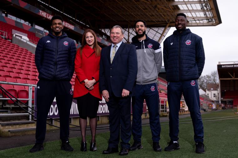 Five people standing side by side in a football stadium