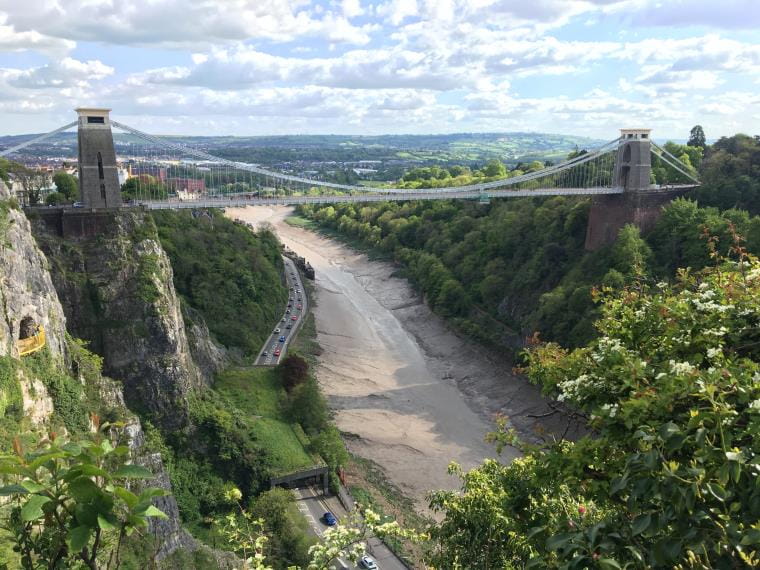 A view of Bristol Suspension Bridge from a far with green trees, river and blue sky