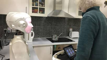 An old man standing in the kitchen with a robot