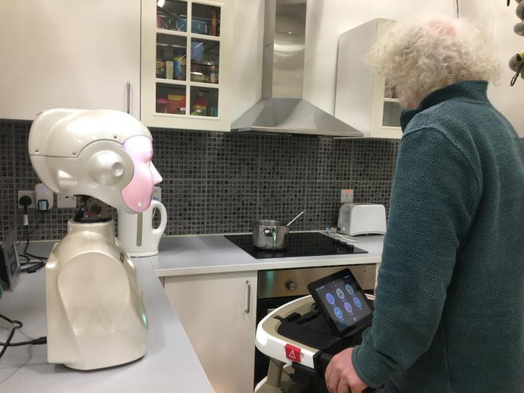 An old man standing in the kitchen with a robot