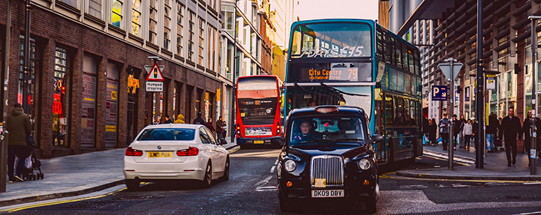 Traffic in a city with cars, buses, people, buildings on both sides of the road, etc.
