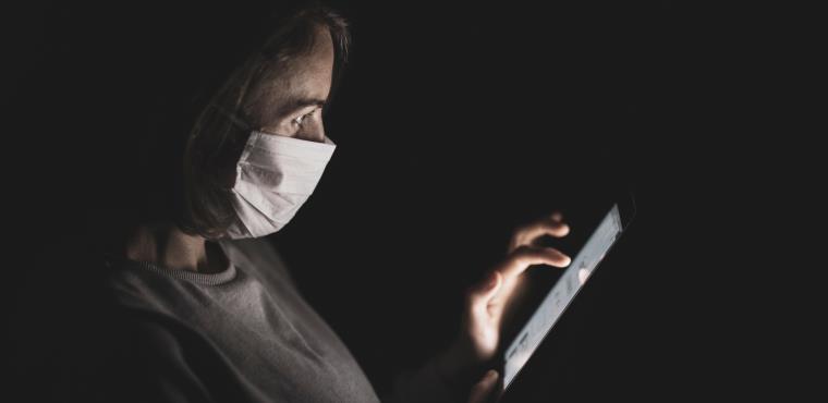 A person wearing medical mask and looking at a tablet's screen