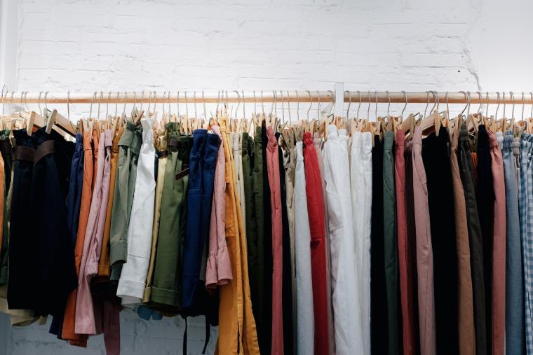 A bunch of trousers with different colours hanging on a hanger bar
